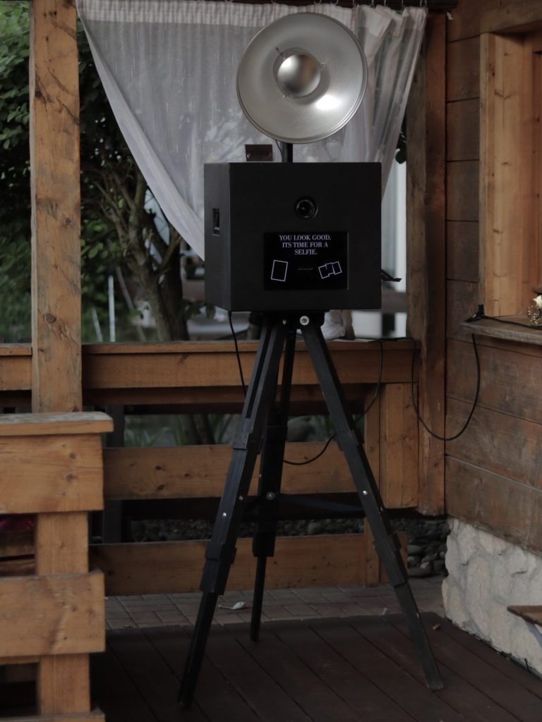 Fotobox schwarz Ein schwarzer Fotobox mit einem großen Blitzlicht auf einem Stativ, umgeben von Dekoration.